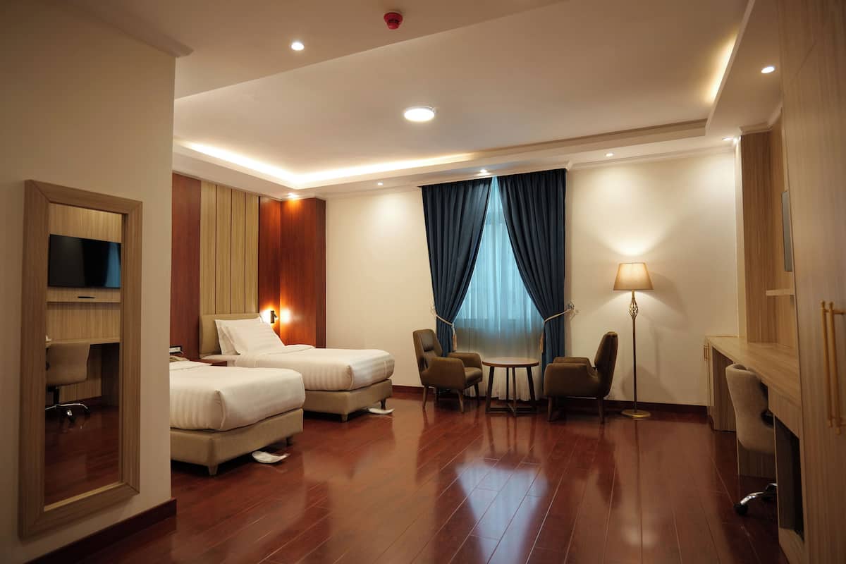 A hotel room with two beds, a desk, a chair, a lamp, and a TV.