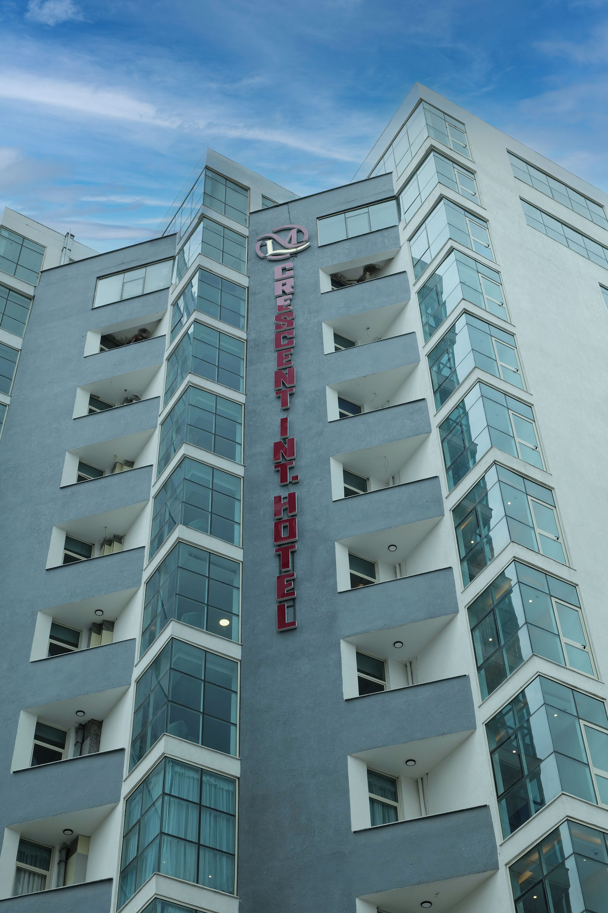 Un hôtel moderne, reconnaissable à son grand panneau vertical indiquant qu’il fait partie du groupe Crescent International Hotels.