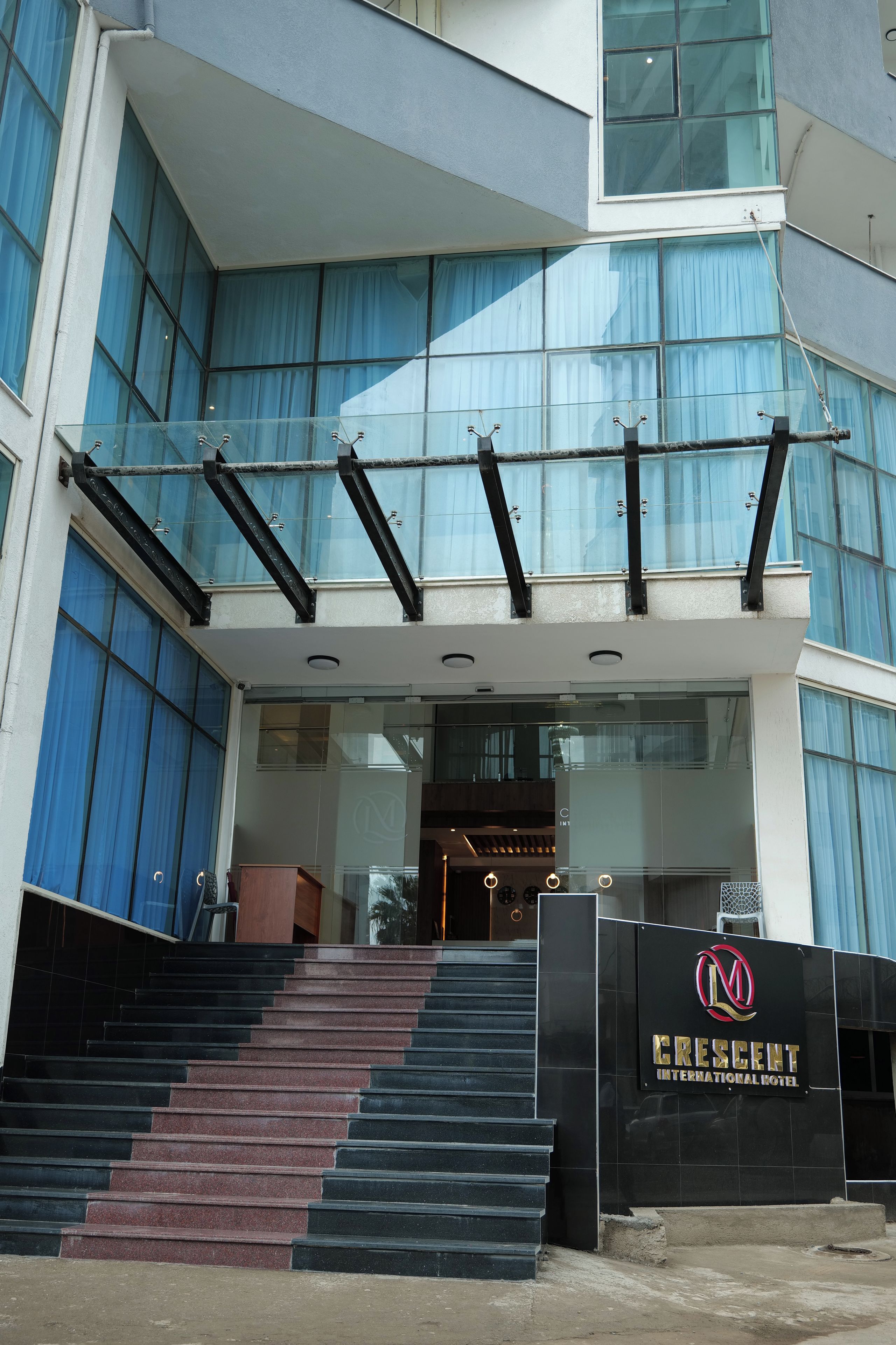 A modern building with a glass facade, a prominent staircase leading to the entrance, and a sign for Crescent International Hotel.