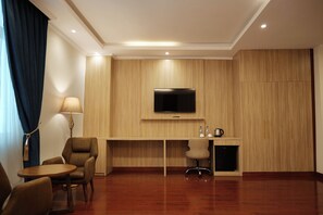 Une chambre d’hôtel avec un mur recouvert de panneaux de bois, un téléviseur à écran plat fixé au-dessus d’un bureau, une chaise, une petite table et une lampe.