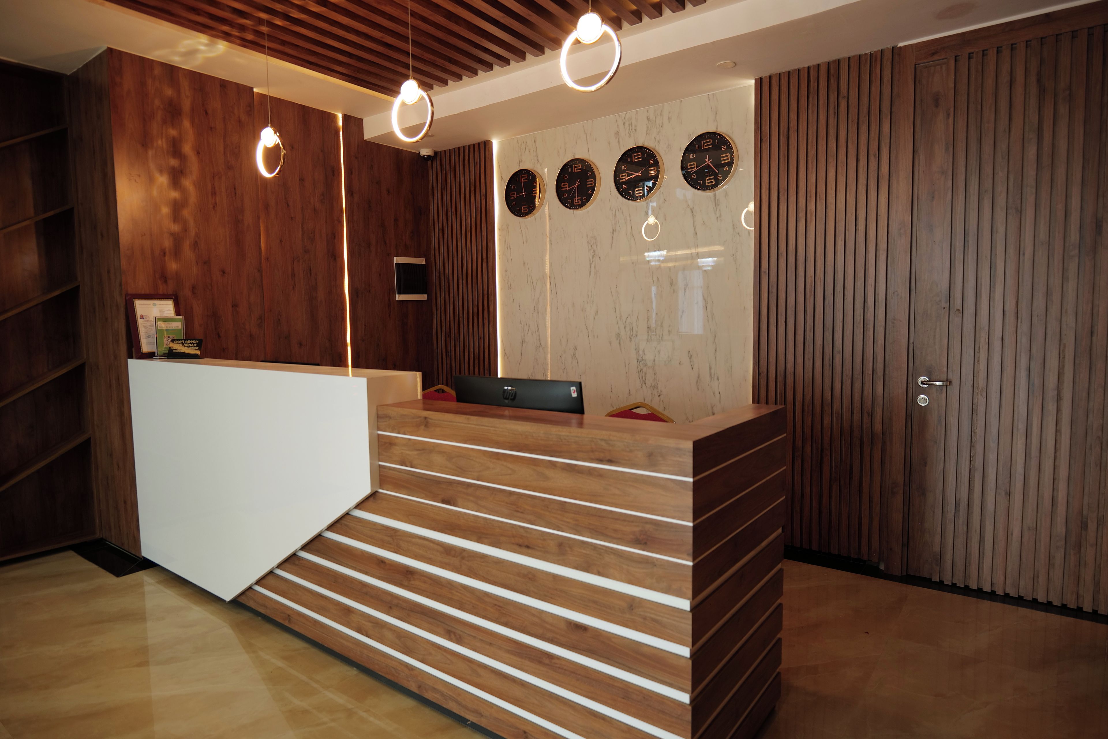 A reception area with a wooden reception desk, a marble wall with clocks, and a wooden slatted wall.