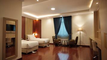 A hotel room with two beds, a desk, a chair, a lamp, and a TV.