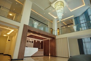 A spacious lobby with a grand chandelier, a wooden reception desk, and a staircase leading to an upper level. - Crescent International Hotel Bole (Addis Ababa)
