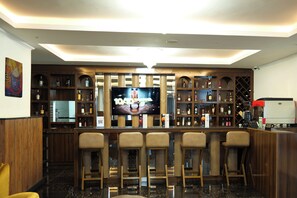 A bar area with a TV screen, wooden shelves with bottles, and bar stools. - Crescent International Hotel Bole (Addis Ababa)