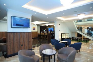Um lobby com área de estar, bar e escadaria.