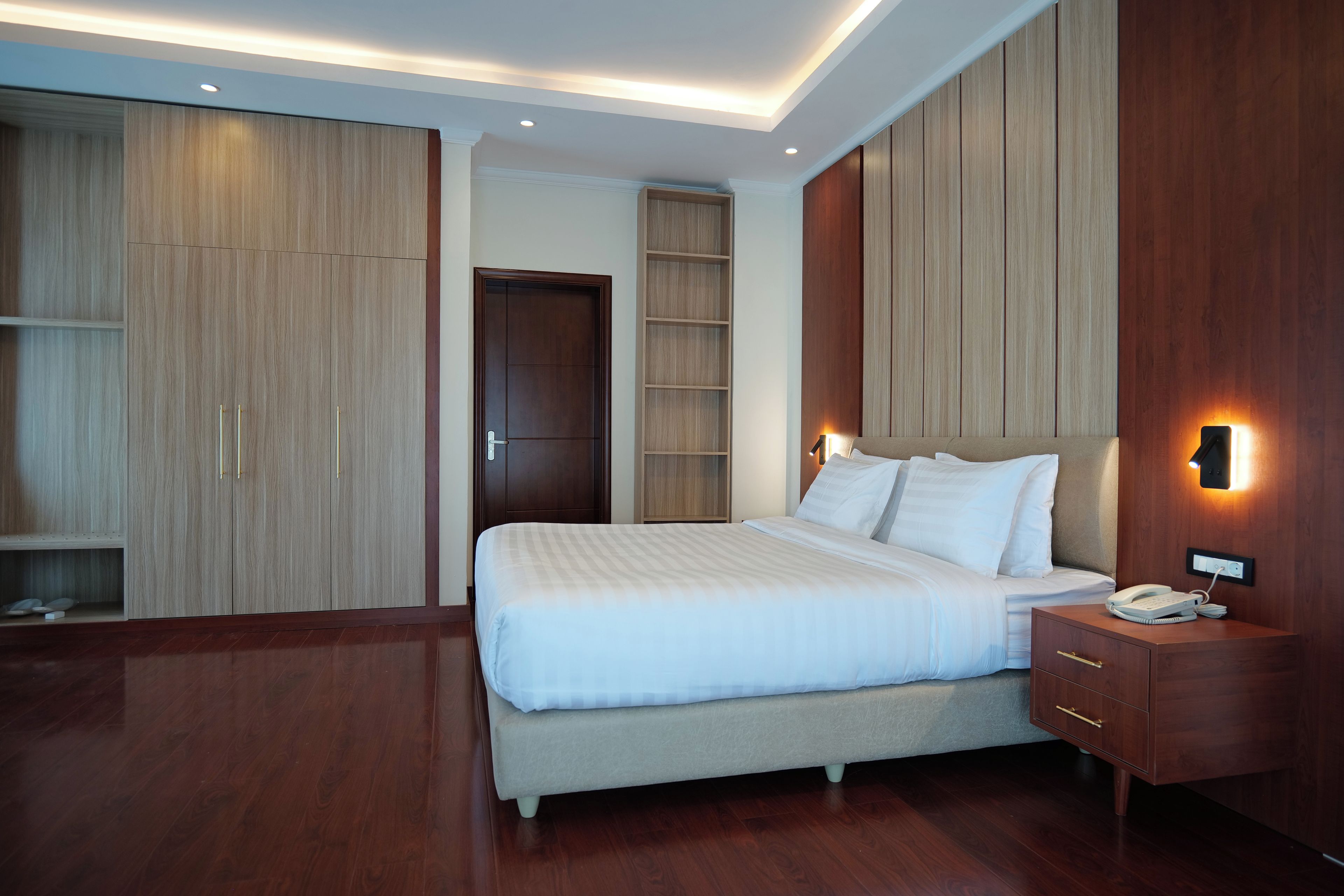 A modern hotel room with a large bed, wooden wardrobe, and built-in shelves.