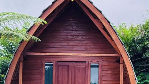 En stuga av trä med en veranda, en staty och en liten trädgårdsdel.