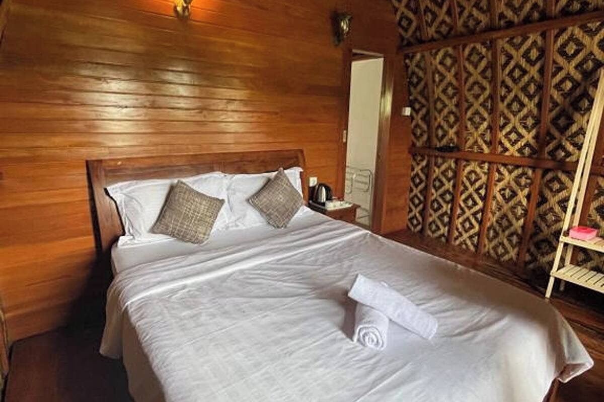 Une pièce en bois avec un lit, une lampe fixée au mur et un papier peint à motifs.