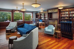 A library with bookshelves, a blue sofa, and a staircase. - Irish Cottege Inn & Suites (Galena)