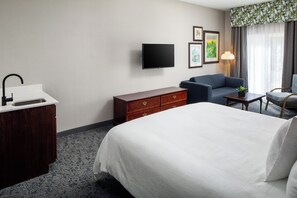 A hotel room with a bed, a desk with a sink, a flat-screen TV, a sofa, a chair, and a lamp. - Irish Cottege Inn & Suites (Galena)