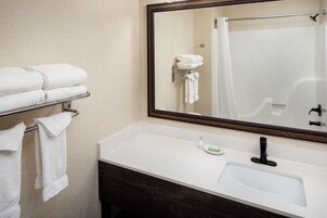 Un baño con un lavabo blanco, un espejo y un perchero con toallas dobladas.