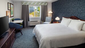 A hotel room with a large bed, a desk with a chair, a TV, and a window with curtains. - Irish Cottege Inn & Suites (Galena)