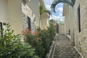 A narrow stone pathway flanked by lush greenery and a building with a stone facade and a wooden door. - Nawan Nusa Dua Bali By Zuzu (Kutuh)
