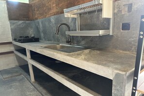 A kitchen with a stainless steel sink, a black portable stove, and a metal rack above the sink. - Nawan Nusa Dua Bali By Zuzu (Kutuh)
