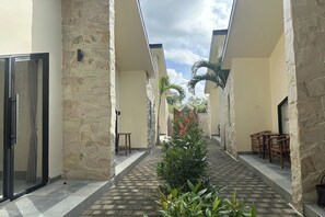 A corridor with stone walls, a central planter, and wooden furniture. - Nawan Nusa Dua Bali By Zuzu (Kutuh)