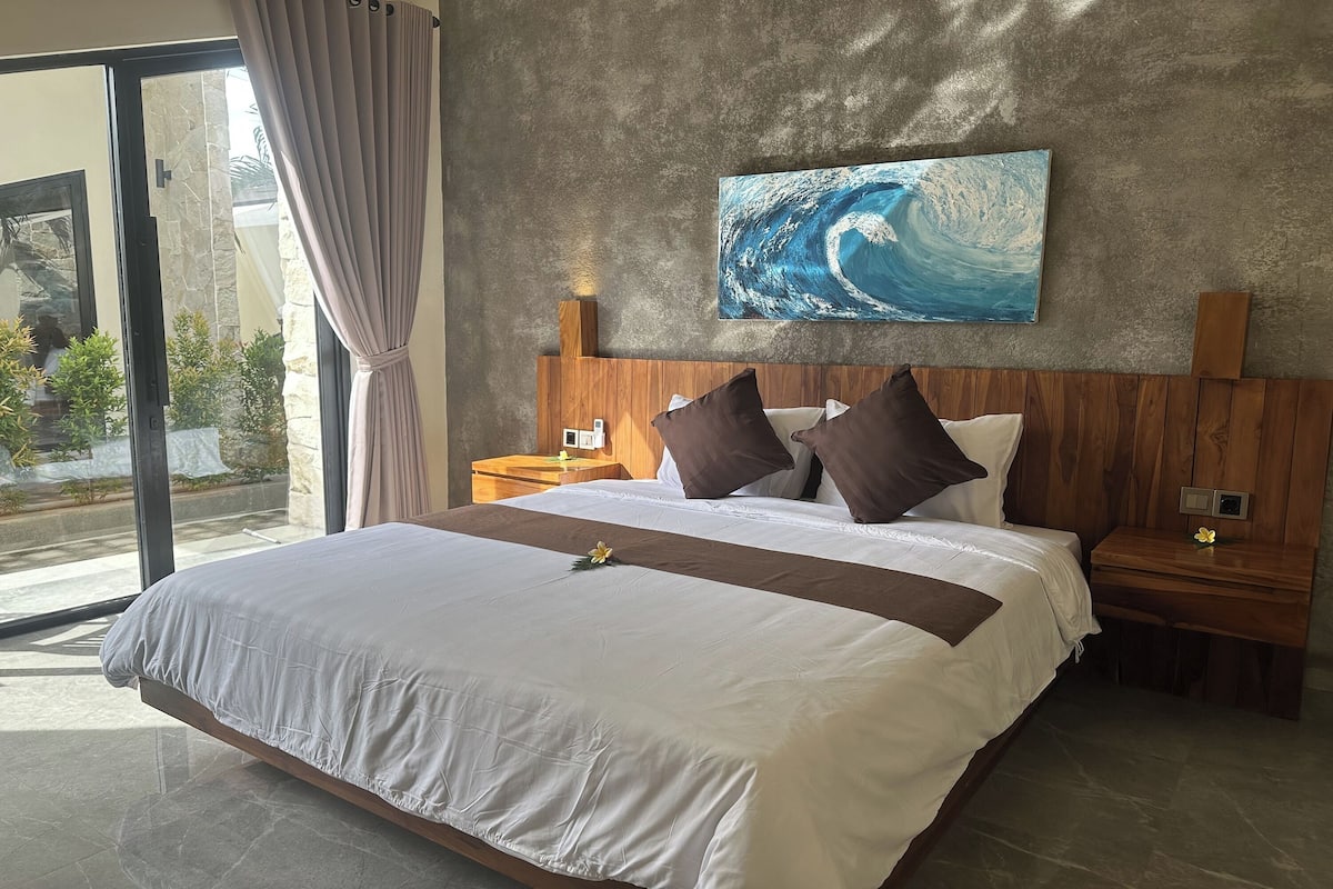 A large bed with a wooden headboard, a nightstand, and a wall-mounted painting of a wave.