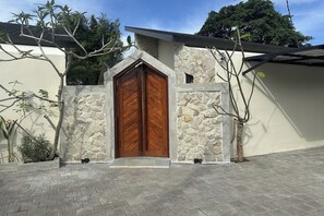 A house with a wooden double door, stone walls, and a paved entrance. - Nawan Nusa Dua Bali By Zuzu (Kutuh)