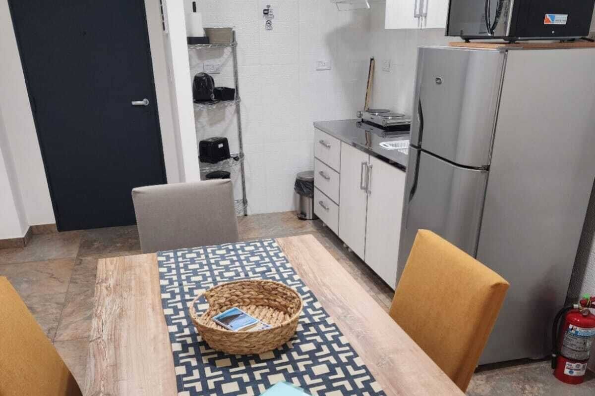 A small kitchenette with a microwave, refrigerator, and cabinets. There's a door marked "SALIDA" and a fire extinguisher near the fridge.