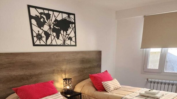A bedroom with two beds, each with a headboard, a world map artwork above the beds, a nightstand with a lamp, and a window with a view. - Comarca Sur (Ushuaia)