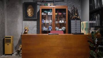 Una stanza con una reception in legno, una statua di Buddha, un mobile contenente oggetti decorativi e una ventola.