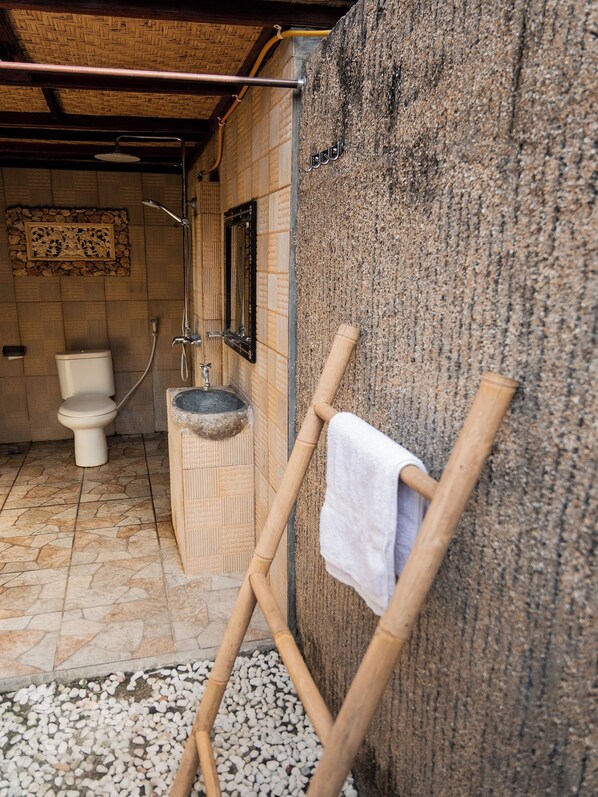 Une salle de bain rustique avec un lavabo en pierre, des toilettes et un espace douche.