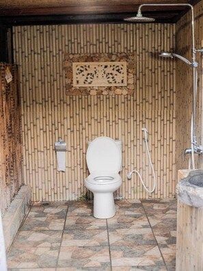 A bathroom with a toilet, shower, and bamboo wall. - Yoki's Bungalows By Zuzu (Kuta)