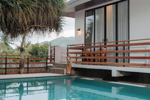 Ein moderner Poolbereich mit Holzterrasse, Statue und Blick auf die Hügel.