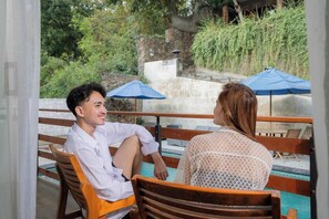 Two people sitting on wooden chairs by a poolside with blue umbrellas. - Yoki's Bungalows By Zuzu (Kuta)