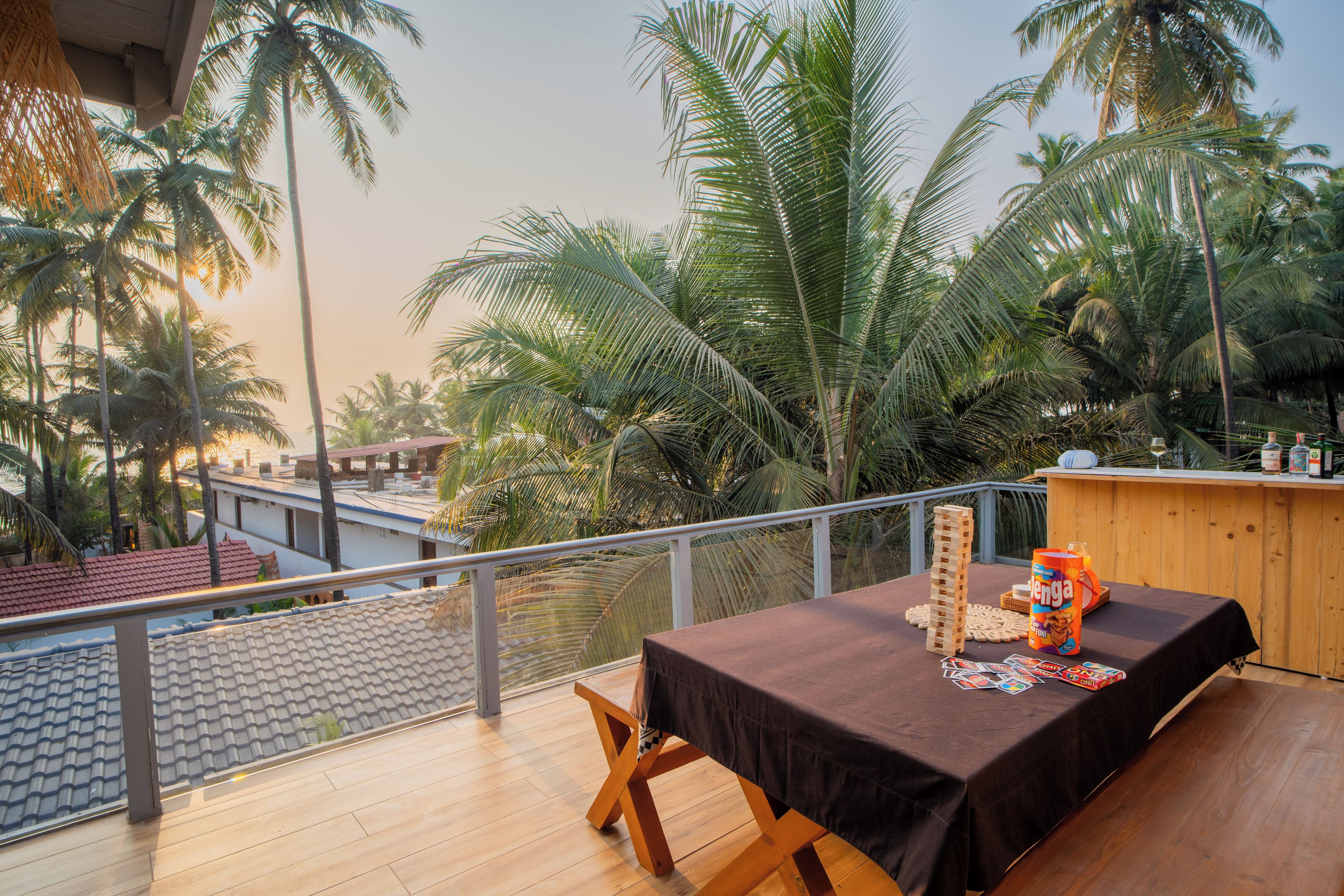 A balcony with a table set for two, overlooking palm trees and a view of a building with a red roof.