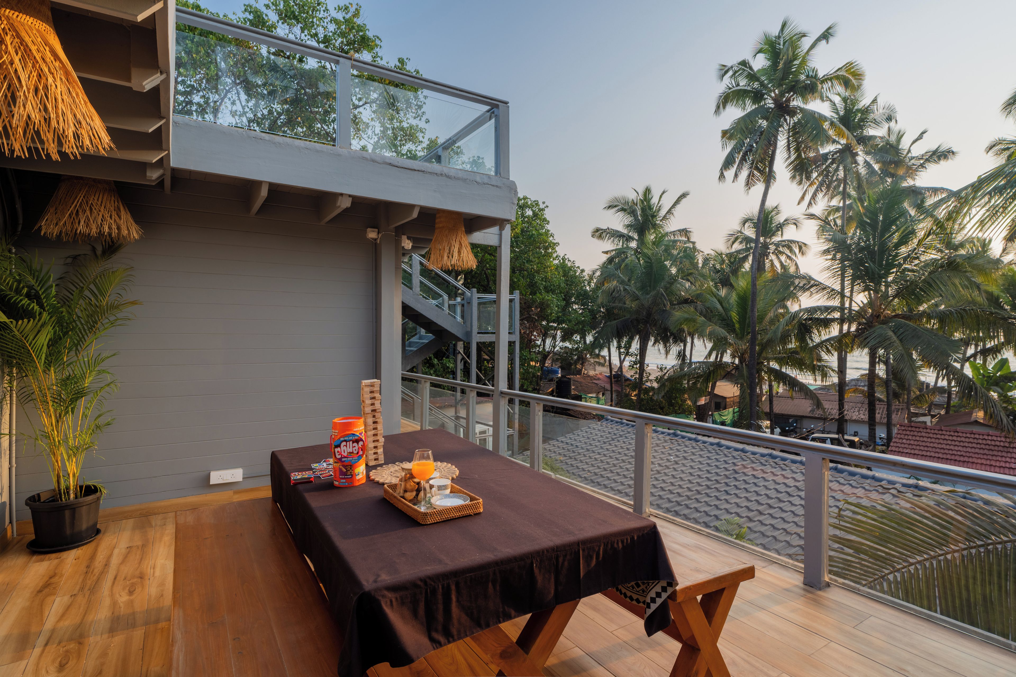 A balcony with a table set for breakfast, overlooking palm trees and a beach.