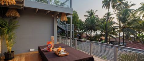 A balcony with a table set for breakfast, overlooking palm trees and a beach.