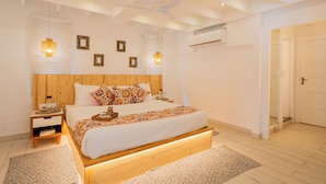 A modern bedroom with a wooden headboard, a large bed with patterned bedding, bedside tables, and wall-mounted lights. - Elivaas House Of Neptune (Morjim)