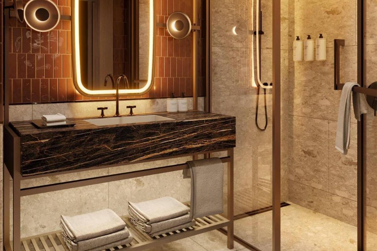 A modern bathroom with a marble sink, a large mirror with illuminated frame, a glass-enclosed shower, and neatly folded towels.