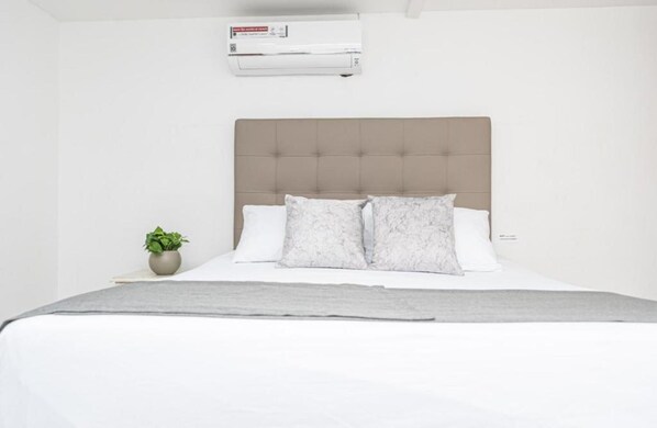Habitación de hotel con cama, cabecero, mesita de noche con una planta y un equipo de aire acondicionado en la pared.