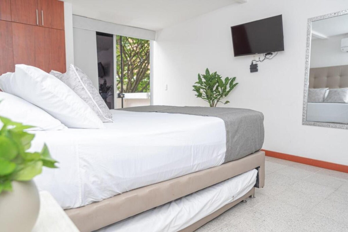 Un dormitorio con una cama, un televisor montado en la pared y una planta en maceta.