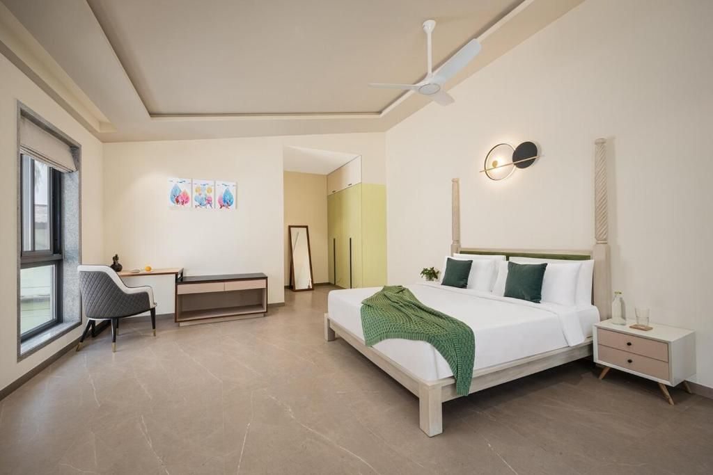 Egy modern szállodai szoba, amelyben található egy ágy, íróasztal, szék és egy mennyezeti ventilátor.