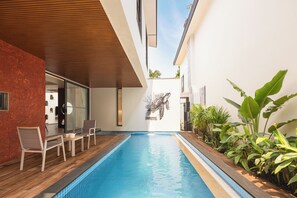 A swimming pool with a wooden deck and lounge chairs, surrounded by plants and a modern architectural design. - Elivaas Cloud 7-luxury Villa In Goa (Vagator)