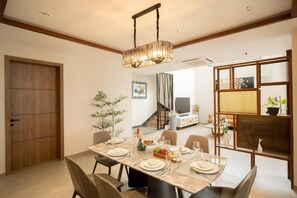 A dining area with a table set for four, a hanging light fixture, and a view into a living room with a staircase. - Elivaas Cloud 7-luxury Villa In Goa (Vagator)