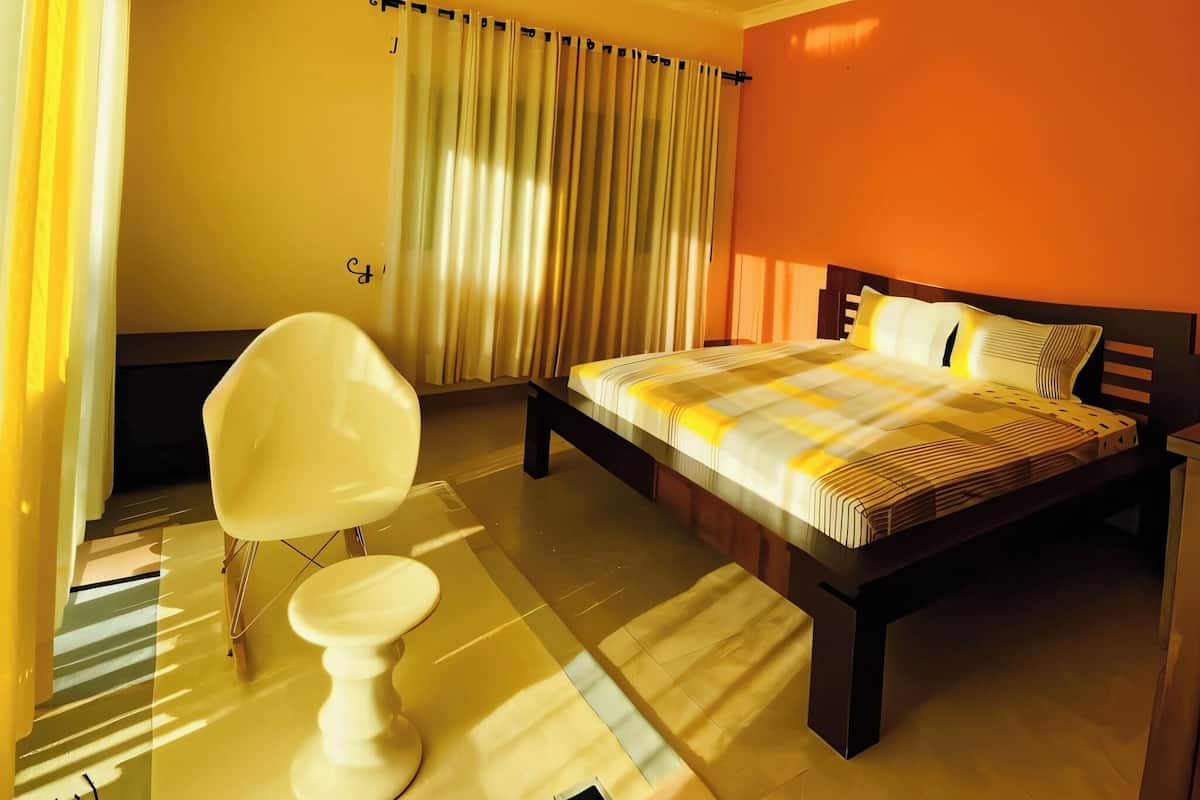A hotel room with a bed, a chair, a toilet, and a window with curtains.