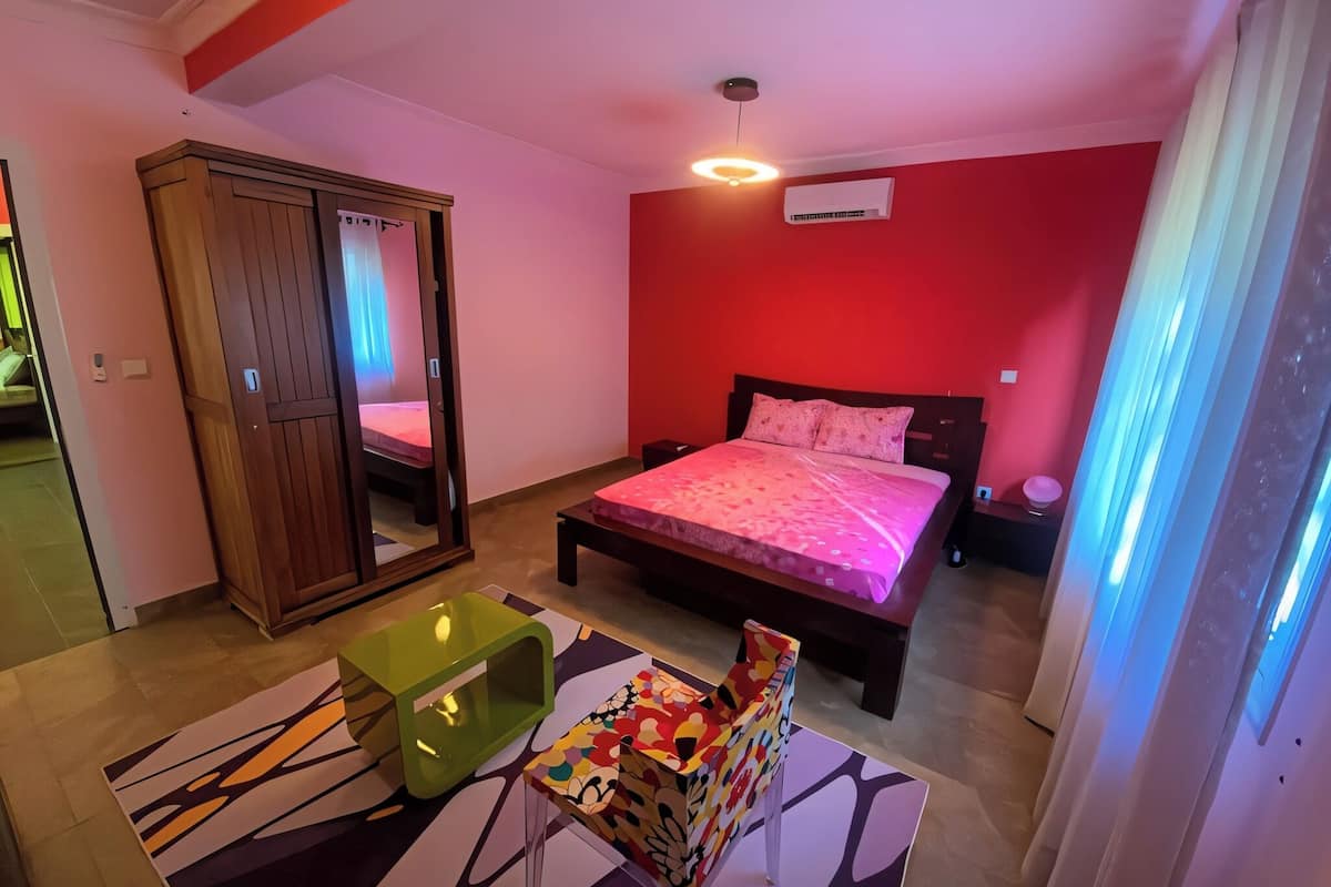 A bedroom with a bed, a wardrobe, a bedside table, a chair, and a window with curtains.