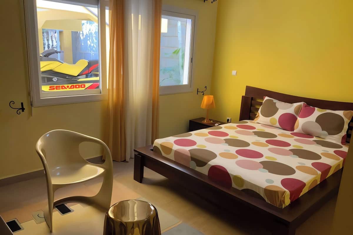 A bedroom with a bed, a chair, a nightstand, and a window with a view of a car and a building.
