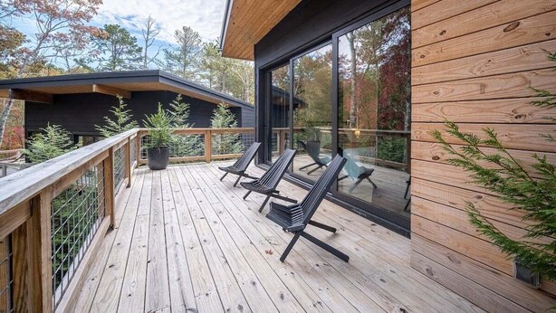 A wooden deck with outdoor seating, a glass wall, and a view of the surrounding trees.