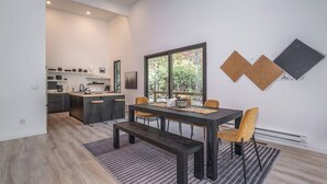 A modern kitchen with dark cabinetry, a central island, and a dining area with a dark table and yellow chairs.