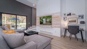 A modern living room with a large TV, grey sofa, and a dining area with a table and chairs.