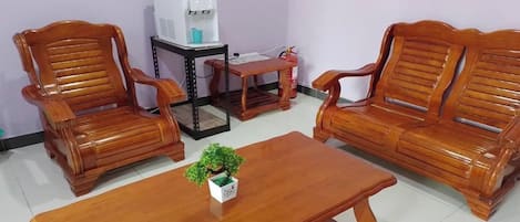 A room with two wooden sofas, a wooden coffee table, and a small table with a water dispenser.
