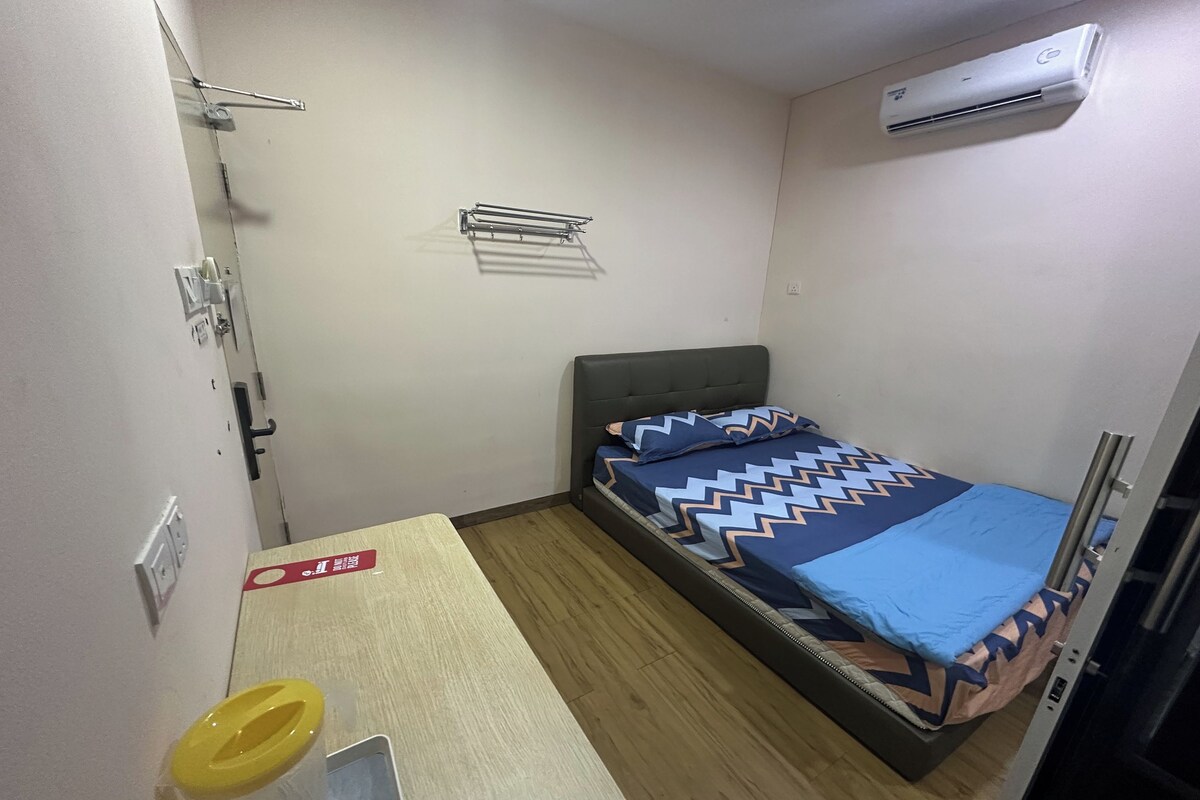 Una stanza piccola e compatta con un letto singolo, un tavolino, una panca, un condizionatore d'aria a parete e un portascopevoli.