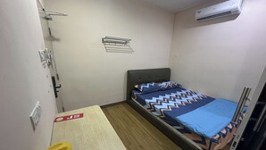 A small, compact room with a single bed, a small table, a bench, a wall-mounted air conditioner, and a towel rack. - Abc Hostel By Zuzu (Seri Kembangan)