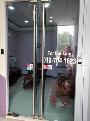 A hotel entrance with a glass door, interior view, and a booking number. - Abc Hostel By Zuzu (Seri Kembangan)