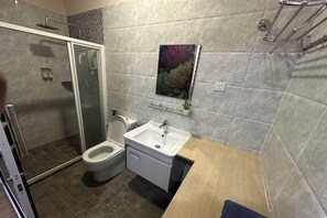 Uma casa de banho moderna com chuveiro, sanita e lavatório.