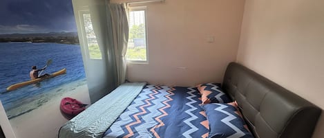 Un dormitorio con cama, ventana, equipo de aire acondicionado y vista de alguien practicando kayak.